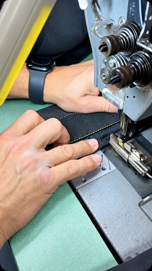 Mani che guidano una fettuccia nera sotto una macchina da cucire industriale