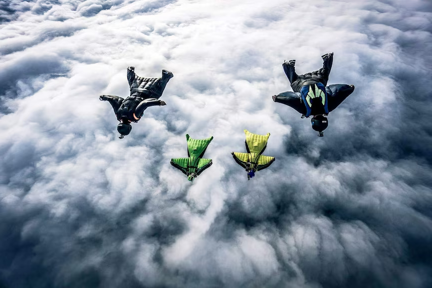 Paracadutista in tuta alare in volo con altri paracadutisti